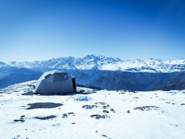 gray dome tent on snow surface overlooking snow capped mountain under blue sky at daytime