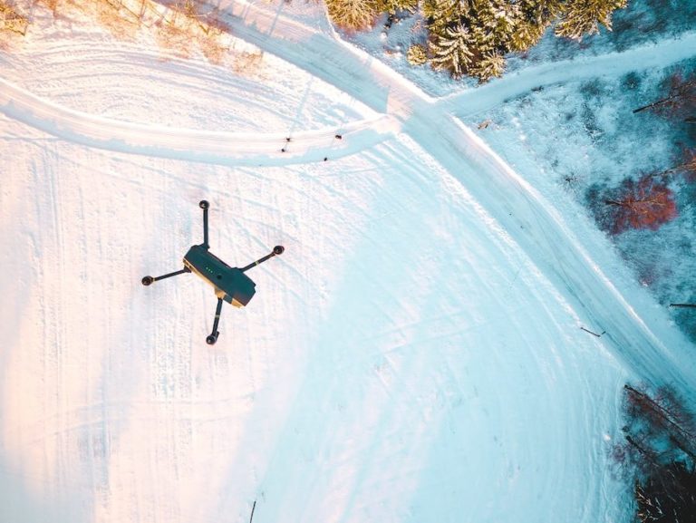 black quadcopter drone flying over snow field during daytime