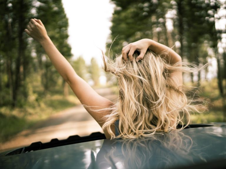 Woman Standing Out Through a Sunroof With Her Hands Up 