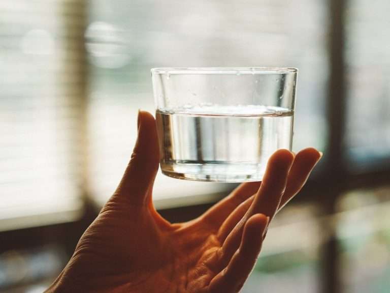 person holding clear glass cup with half-filled water