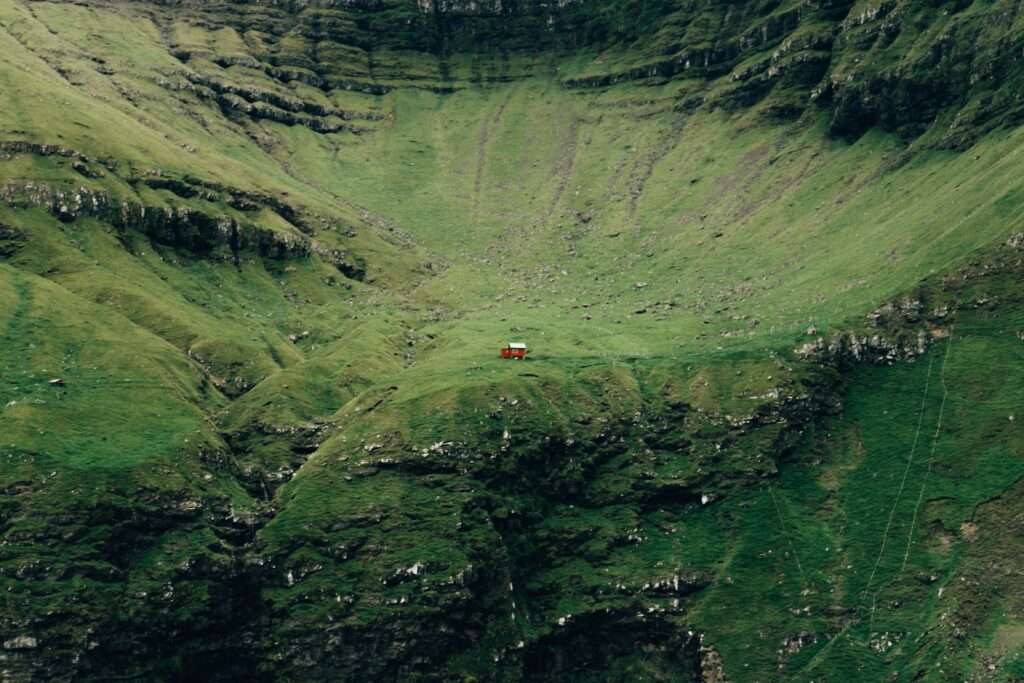 red car on road in between green mountains during daytime